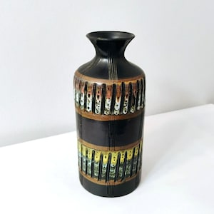May include: A black ceramic vase with a narrow neck and a wide body. The vase features horizontal bands of color, including brown, yellow, and green, with vertical striped detailing. The vase is approximately 12 inches tall.