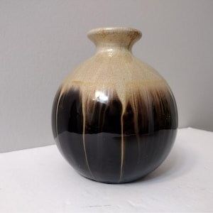 May include: A small, round ceramic vase with a brown and beige glaze. The vase has a wide mouth and a narrow neck.