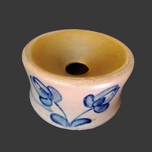 May include: A small, ceramic bowl with a light pink exterior and a yellow interior. The bowl features blue floral designs and a central hole. The design is reminiscent of vintage pottery.