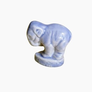May include: A small, light blue ceramic elephant figurine. The elephant is standing on a small base, with its trunk down and ears visible. The figurine is made in England.
