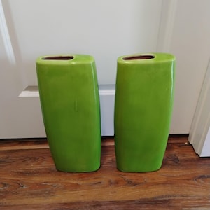 May include: Two tall, rectangular ceramic vases with a vibrant lime green glazed finish. Each vase features a smooth, slightly curved silhouette with a narrow, oval-shaped opening at the top, showcasing a consistent, glossy, solid green color throughout.