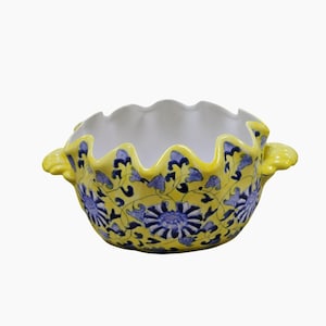Peut inclure: Un bol en céramique avec un extérieur jaune vif orné d'un motif floral bleu et un intérieur blanc. Le bol présente un bord festonné et deux petites anses jaunes en forme de coquille sur les côtés, offrant un design décoratif et fonctionnel.