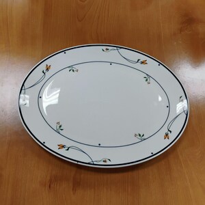 May include: An oval white ceramic serving platter featuring a thin dark blue border and a delicate pattern of small orange tulip-like flowers with green stems and leaves scattered across the rim and the center of the dish.