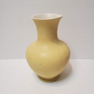 May include: A pale yellow ceramic vase with a bulbous body and a flared neck. The interior of the vase is white. The vase has a round base and a smooth, matte finish. A decorative piece for the home.