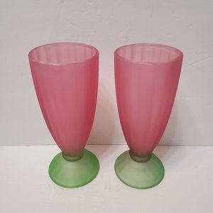 Könnte beinhalten: Zwei Vintage-Eisbecher aus rosa und grün gefrostetem Glas. Die hohen, tulpenförmigen Gläser haben einen rosafarbenen Körper und einen grünen Sockel. Die Gläser sind ideal zum Servieren von Eis-Sodas oder Milchshakes.