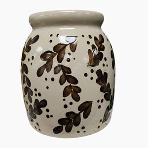 May include: A cream-coloured ceramic jar with a wide base and a slightly narrower top. The jar is decorated with brown leaf patterns and small dots. The rim of the jar is a lighter cream colour.