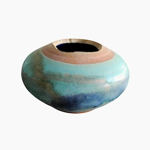 Puede incluir: Un jarrón de cerámica hecho a mano con una forma redondeada y orgánica. El jarrón presenta una paleta de colores de tonos turquesa, marrón y azul. La abertura es azul oscuro y el exterior tiene un acabado texturizado y vidriado. Es un artículo decorativo.