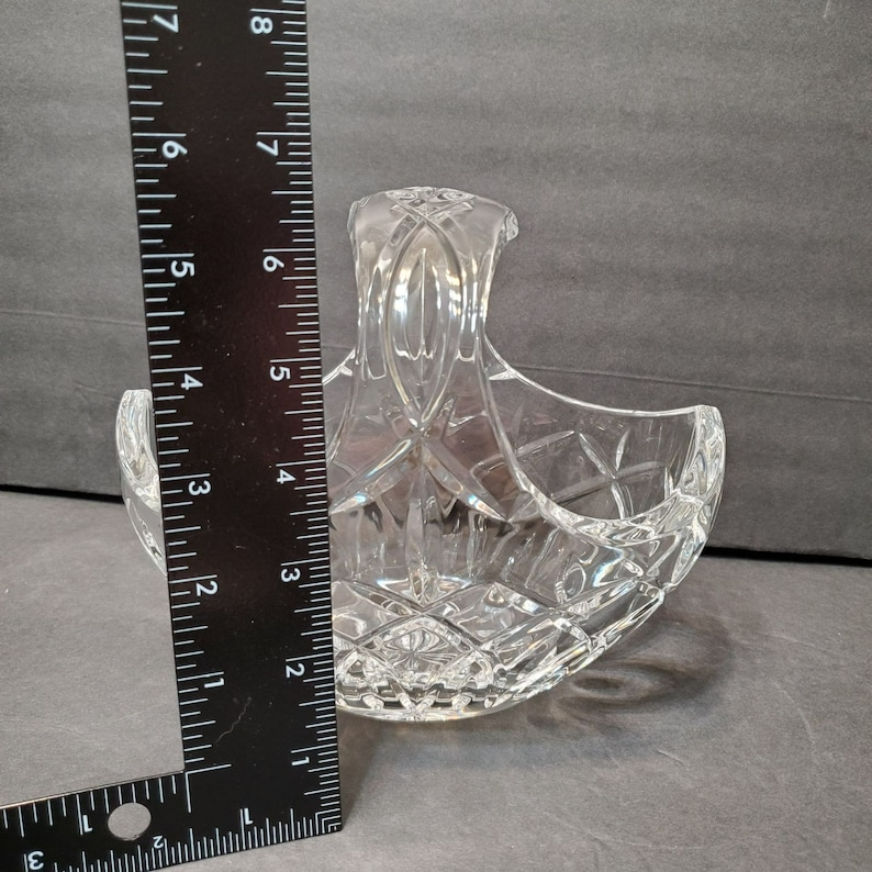 Pu&ograve; includere: Un cestino di cristallo trasparente con manico, con un motivo a diamante. Il cestino &egrave; alto circa 15 cm, misurato con un righello nero. Il cestino &egrave; progettato con una forma curva e un manico decorativo.