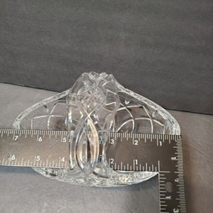 Pu&ograve; includere: Un cestino di vetro tagliato trasparente con manico. Il cestino ha un motivo a diamante ed &egrave; lungo circa 15 cm. Il manico &egrave; finemente decorato. Il cestino &egrave; su una superficie grigia.