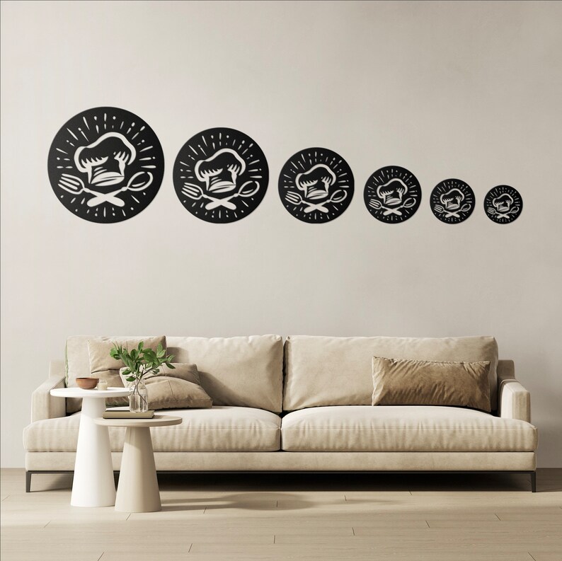 May include: Six black metal wall art pieces, each with a chef's hat, fork, and spoon design. The circular pieces are of varying sizes and are mounted on a neutral wall above a beige sofa. The design is suitable for a kitchen or dining room.