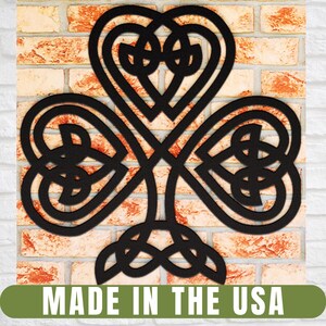 May include: Black metal shamrock wall art with Celtic knot design. The three-leaf clover is mounted on a brick wall. The text "MADE IN THE USA" is displayed at the bottom.
