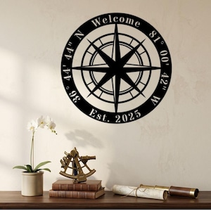 May include: Black metal compass rose wall art with the word "Welcome" at the top and "Est. 2025" at the bottom. The compass rose has directional coordinates around the edge. A potted orchid, books, and a telescope are on a wooden surface below.