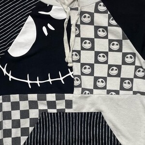 May include: Black and white hooded sweatshirt with a patchwork design featuring a stitched-up Jack Skellington face, checkered pattern, and stripes.