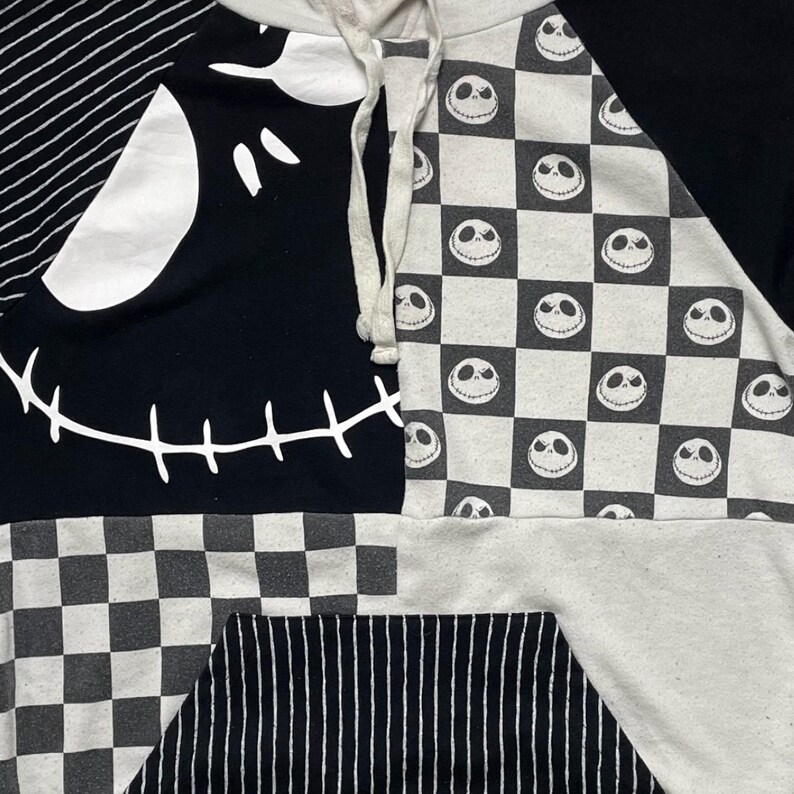 May include: Black and white hooded sweatshirt with a patchwork design featuring a stitched-up Jack Skellington face, checkered pattern, and stripes.