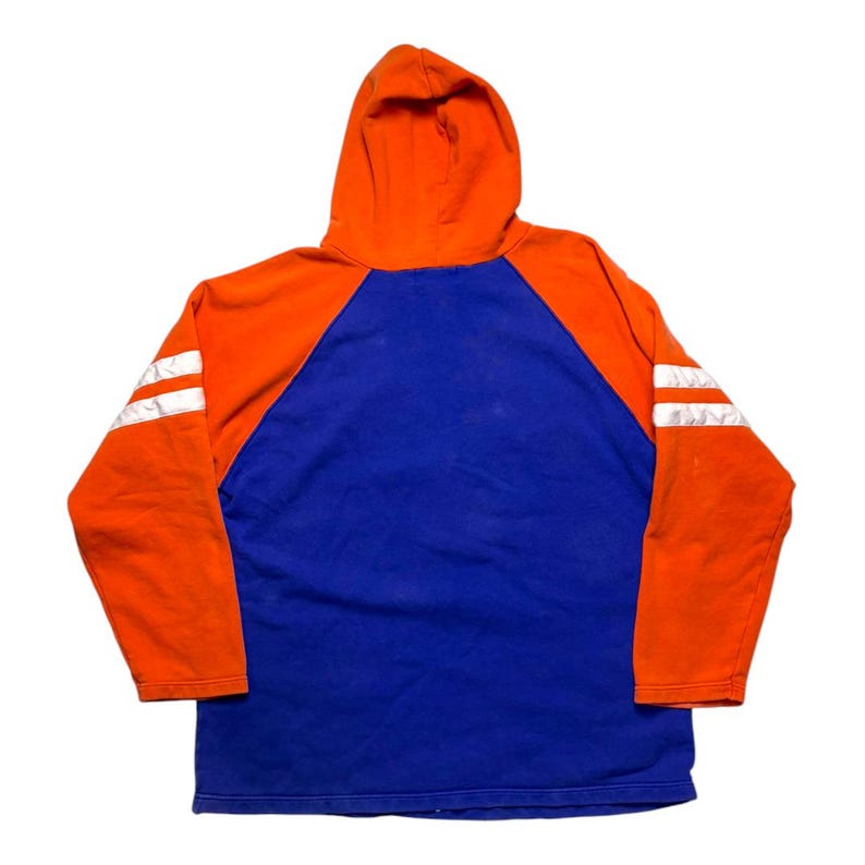 May include: A long-sleeve hoodie featuring a vibrant orange hood and sleeves contrasted with a solid blue torso. The sleeves are accented with two horizontal white stripes. The garment is constructed with raglan-style sleeves and a hood.