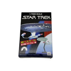 May include: A rectangular product box for a 1/7000 scale Star Trek model kit. The black packaging features the Star Trek logo, images of a starship, red vertical stripes, the Paramount Pictures logo, and Japanese text including 統一スケール全10種+?ワープVer.1種.