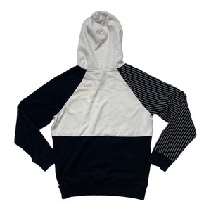 May include: A black and white striped hoodie with a white hood and a black and white striped sleeve. The hoodie has a black bottom and a white middle section.