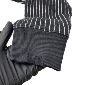 May include: Close-up of the black and white striped cuff of a long-sleeved shirt. The cuff is made of a soft, stretchy fabric and has a ribbed texture.