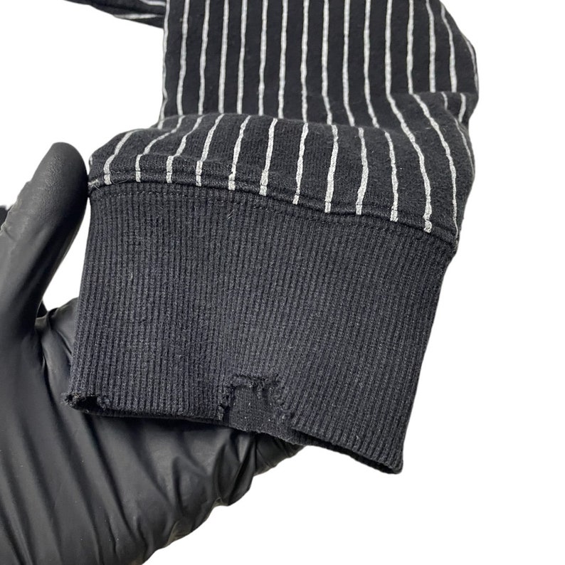 May include: Close-up of the black and white striped cuff of a long-sleeved shirt. The cuff is made of a soft, stretchy fabric and has a ribbed texture.