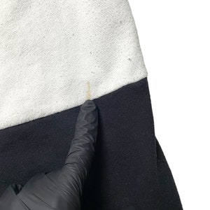 May include: Close-up of a black and white sweatshirt. The sweatshirt has a white top and a black bottom. There is a small yellow stain on the white part of the sweatshirt.