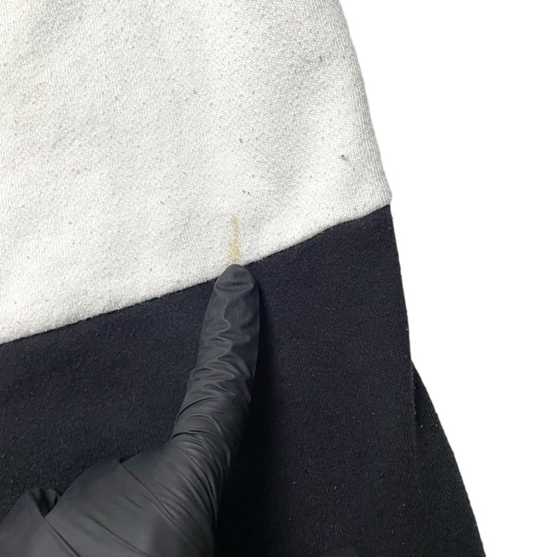 May include: Close-up of a black and white sweatshirt. The sweatshirt has a white top and a black bottom. There is a small yellow stain on the white part of the sweatshirt.