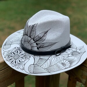 May include: A white straw hat with a black leather band and a black and white design of flowers and birds.