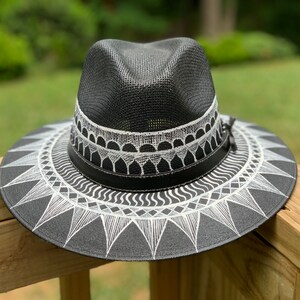 May include: A black straw hat with a white geometric design. The hat has a wide brim and a band around the crown.