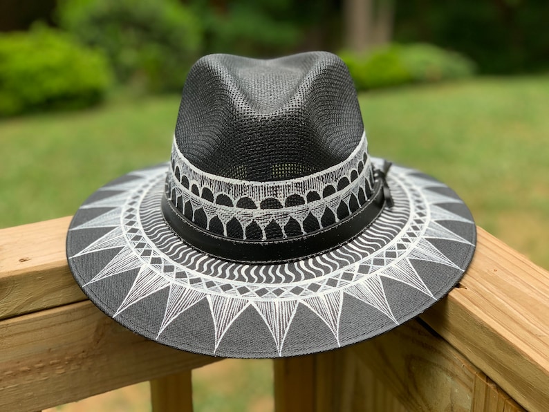 May include: A black straw hat with a white geometric design. The hat has a wide brim and a band around the crown.