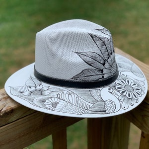 May include: A white straw hat with a black band and black ink drawings of birds, flowers, and leaves.