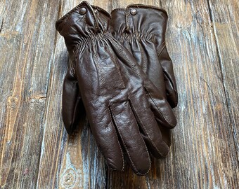May include: A pair of brown leather gloves with a textured surface. The gloves have a button detail on the wrist.