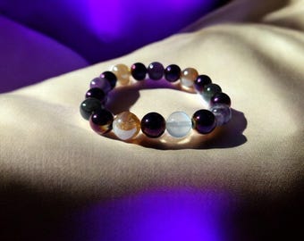 May include: A multi-colored beaded bracelet with purple, brown, and white beads. The bracelet is made of round beads and has a metallic sheen.