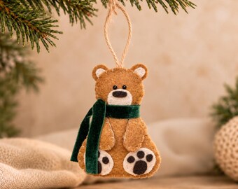 May include: A brown felt bear ornament featuring a dark green velvet scarf, white felt muzzle and paw pads, and black stitched details. The bear has a jute twine loop for hanging and is constructed with visible light-colored blanket stitching.