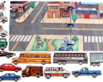 May include: A collection of miniature toy vehicles and figures, including a school bus, truck, cars, and people on bicycles, set against a painted backdrop of a town with buildings and streets.