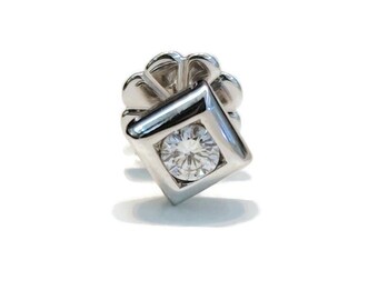 May include: A silver-toned stud earring featuring a square-shaped setting with a single round, clear, faceted gemstone at the center. The earring includes a secure, petal-shaped metal backing mechanism visible behind the main square frame.