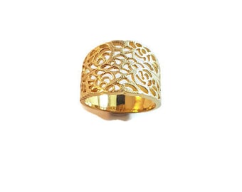 May include: A wide gold band ring featuring an intricate, openwork filigree design composed of repeating floral rose patterns. The metal has a polished, reflective finish, and the band maintains a consistent width throughout its circular structure.