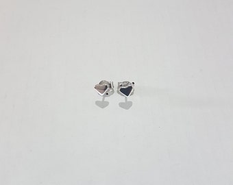 May include: A pair of small silver stud earrings shaped like hearts. Each earring features a polished metallic finish with a smooth surface and a post backing. The earrings are positioned side by side, reflecting light on their curved edges.