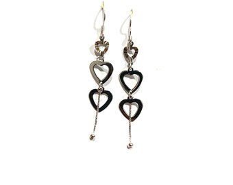 May include: A pair of silver-toned drop earrings featuring a vertical arrangement of three open heart-shaped links of varying sizes. The earrings hang from thin silver chains and terminate in small, polished spherical beads at the bottom ends.