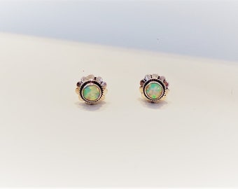 May include: A pair of stud earrings featuring round, iridescent opal cabochons set in gold-toned metal. Each earring has a scalloped, petal-like border surrounding the central stone, creating a flower-inspired shape with a polished finish.