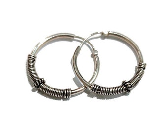 May include: A pair of silver hoop earrings featuring a smooth circular band accented with segments of coiled wire detailing. The metallic surface has a polished finish with darkened recessed areas that highlight the textured wire wrapping.