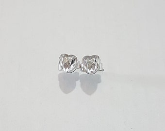 May include: A pair of silver-toned stud earrings shaped like hearts. Each earring features a faceted, reflective surface that creates a multi-dimensional appearance. The studs are designed with a polished metallic finish and include standard earring backs.