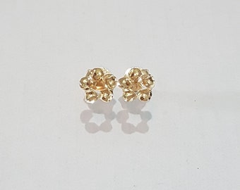 May include: A pair of gold stud earrings shaped like five-petaled flowers. Each earring features a polished metallic finish with rounded petals radiating from a central point, creating a small, symmetrical floral design that reflects light.