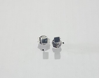 May include: A pair of small, square-shaped stud earrings with a polished silver-tone finish. Each earring features a flat, dark square face and a secure metal backing. The backs are clearly stamped with the number 750, indicating the metal purity.