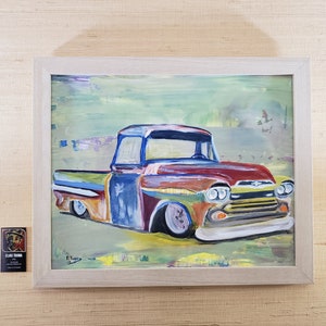 May include: A colorful painting of a vintage pickup truck with a green, yellow, blue, and red color scheme. The truck is painted in a stylized, abstract style. The painting is framed in a light wood frame.