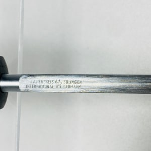 May include: Close-up of a metal object with the text "J.A. Henckels International Solingen Germany". The object has a dark handle and a silver-colored shaft. The text is in a rectangular shape.