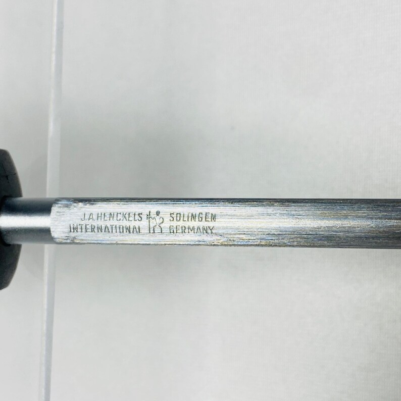 May include: Close-up of a metal object with the text "J.A. Henckels International Solingen Germany". The object has a dark handle and a silver-colored shaft. The text is in a rectangular shape.