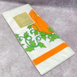 May include: A white Party Papers soft crepe tablecloth with a Halloween pumpkin design. The tablecloth is 152 cm by 259 cm and features an orange pumpkin, green vines, and an orange stripe.