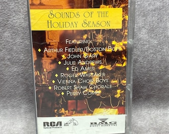 May include: A cassette tape with a Christmas tree design and the text "Sounds of the Holiday Season". The cassette features artists such as Arthur Fiedler, John Gary, Julie Andrews, Roger Whittaker, Vienna Choir Boys, Robert Shaw Chorale, and Perry Como. The cassette is labeled with RCA Special Products and BMG Direct Marketing.