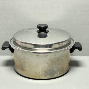 Puede incluir: Olla de cocina de acero inoxidable con tapa y asas negras. La olla tiene un acabado plateado y un pomo negro en la tapa. La olla está diseñada para cocinar y tiene un diseño clásico y funcional.