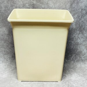 May include: A rectangular, cream-colored wastebasket with a slightly flared top. The wastebasket has a smooth, matte finish and a simple, modern design. The interior is not visible.