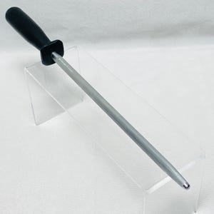 May include: A knife sharpening steel with a black handle and a silver steel rod. The rod is cylindrical and tapers to a point. The handle is square and connects to the rod. The product is designed for sharpening knives.